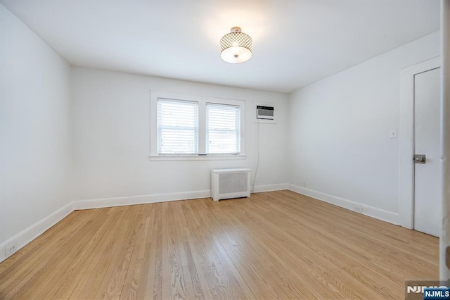 spare room with radiator, light hardwood / wood-style flooring, and a wall mounted AC