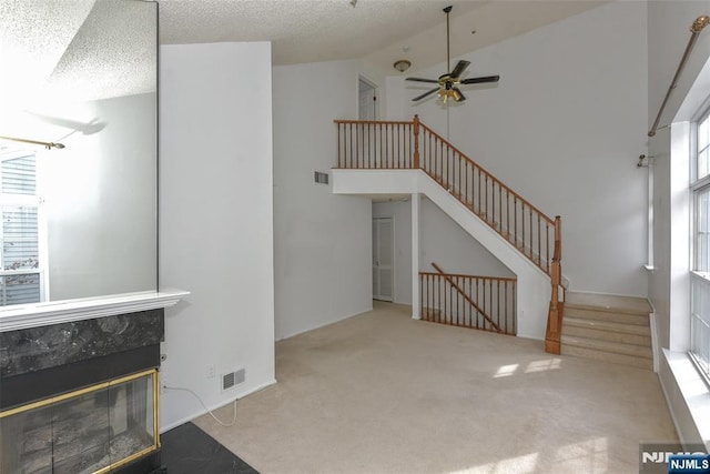 unfurnished living room featuring visible vents, light carpet, a tiled fireplace, and stairs