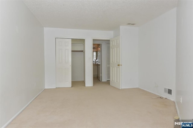 unfurnished bedroom featuring baseboards, visible vents, a textured ceiling, and light colored carpet