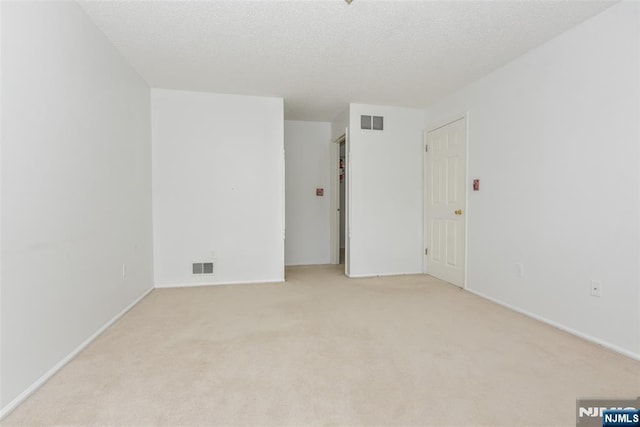 spare room with light carpet, a textured ceiling, and visible vents