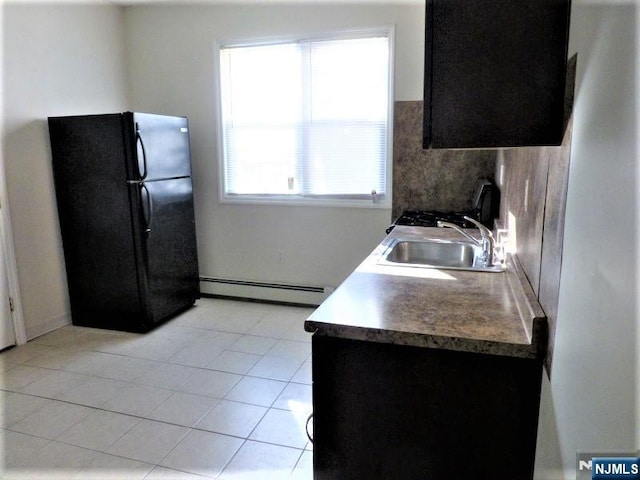 kitchen featuring sink, light tile patterned floors, black refrigerator, decorative backsplash, and a baseboard heating unit