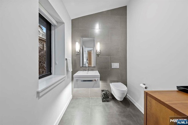 bathroom featuring tile patterned floors, toilet, vaulted ceiling, tile walls, and vanity