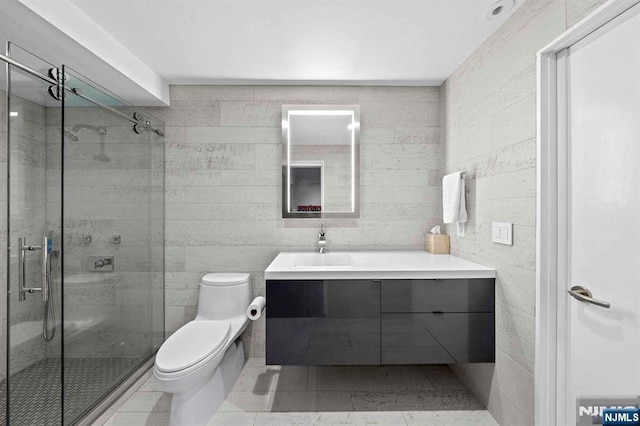 bathroom featuring a shower with door, tile walls, vanity, tile patterned floors, and toilet