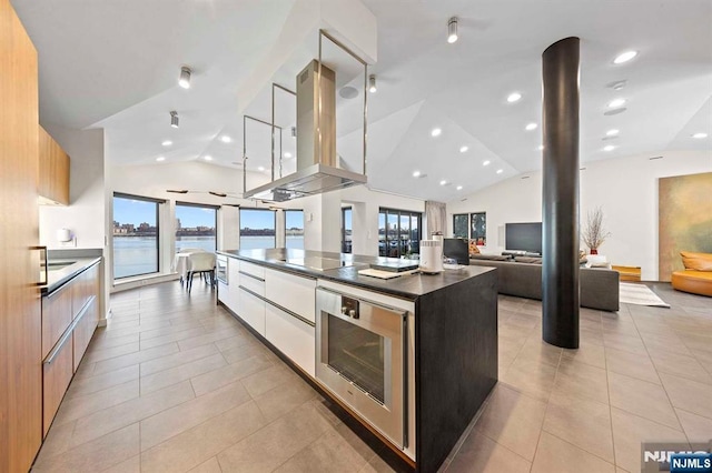 kitchen with island range hood, white cabinetry, lofted ceiling, light tile patterned floors, and a spacious island