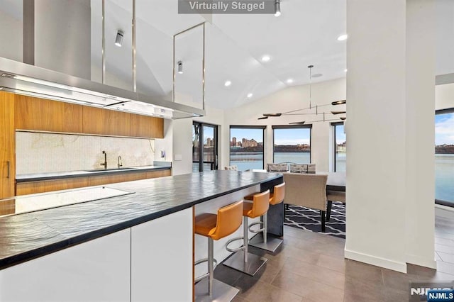 kitchen featuring stovetop, sink, a water view, white cabinetry, and a kitchen breakfast bar