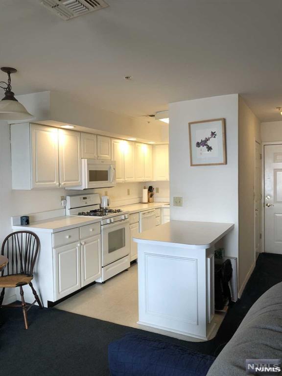 kitchen featuring white appliances, visible vents, white cabinets, light countertops, and hanging light fixtures