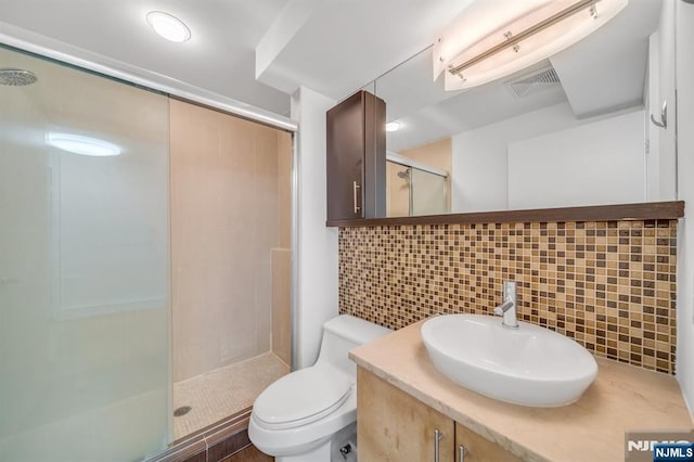 bathroom featuring a shower with door, toilet, vanity, and decorative backsplash