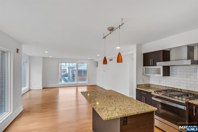 kitchen with stainless steel gas stove, a center island, dark brown cabinets, decorative backsplash, and wall chimney range hood