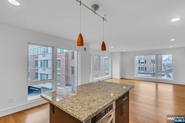 kitchen featuring light hardwood / wood-style flooring, oven, light stone counters, and decorative light fixtures