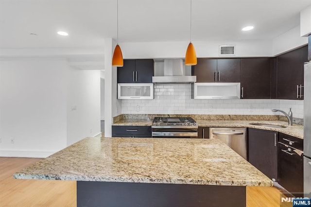 kitchen featuring pendant lighting, sink, stainless steel appliances, wall chimney range hood, and light hardwood / wood-style flooring