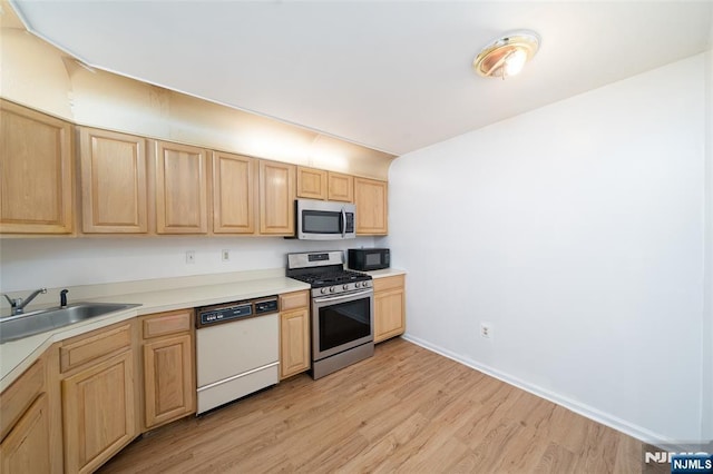 kitchen featuring light wood finished floors, stainless steel appliances, light countertops, light brown cabinets, and a sink