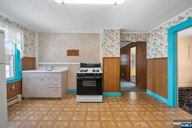 kitchen featuring gas stove, crown molding, wooden walls, and a baseboard radiator