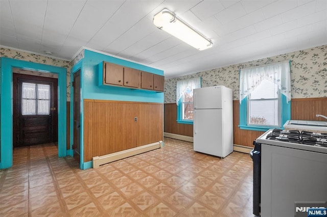 kitchen with a baseboard heating unit, plenty of natural light, range with gas stovetop, and white fridge