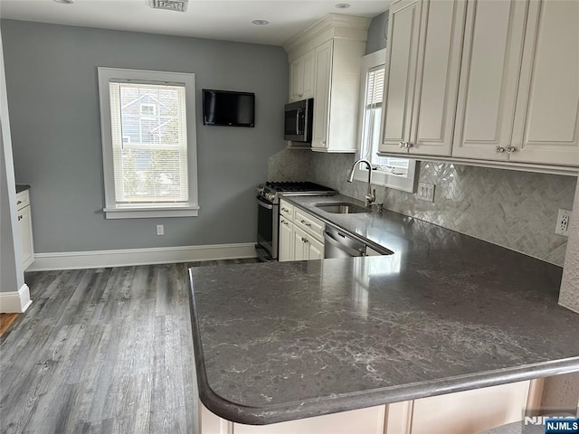 kitchen with sink, dark wood-type flooring, stainless steel appliances, tasteful backsplash, and kitchen peninsula