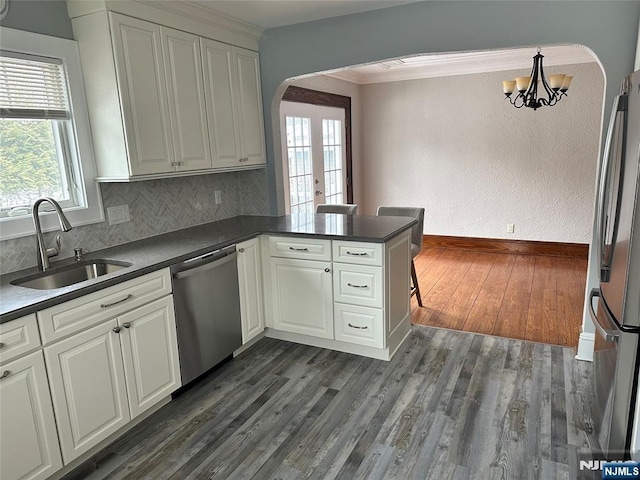 kitchen with sink, appliances with stainless steel finishes, ornamental molding, dark hardwood / wood-style flooring, and kitchen peninsula