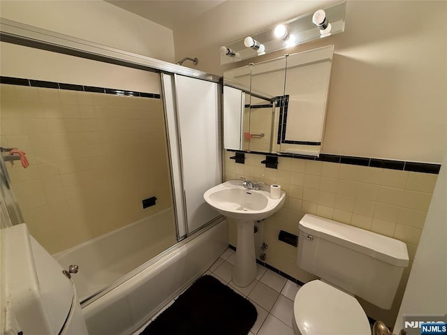 bathroom featuring tile patterned flooring, combined bath / shower with glass door, toilet, and tile walls