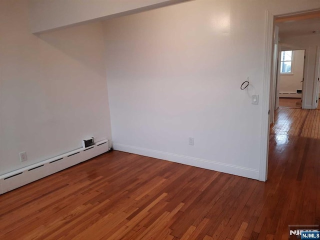 spare room featuring a baseboard heating unit and hardwood / wood-style flooring