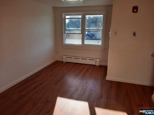 empty room featuring dark hardwood / wood-style flooring and a baseboard heating unit