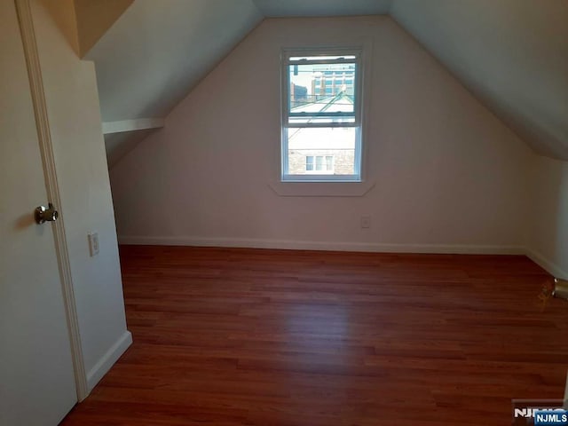 additional living space featuring dark wood-type flooring and vaulted ceiling