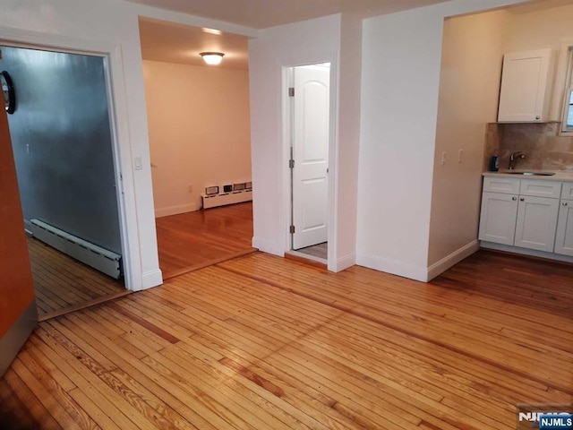 unfurnished dining area featuring sink, light hardwood / wood-style floors, and a baseboard heating unit