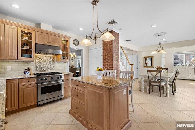 kitchen featuring hanging light fixtures, ventilation hood, high end stainless steel range, light stone countertops, and glass insert cabinets