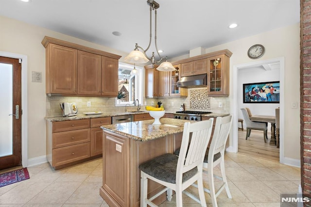 kitchen with a center island, hanging light fixtures, glass insert cabinets, a sink, and under cabinet range hood