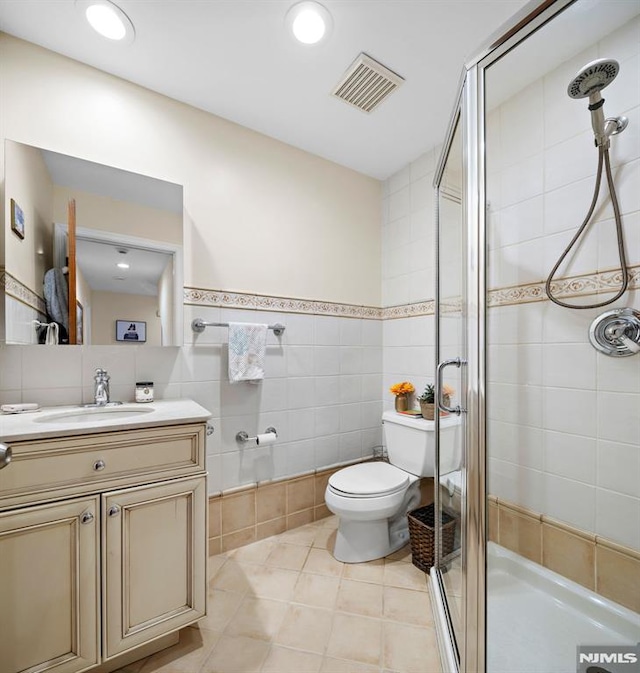 full bathroom featuring toilet, vanity, visible vents, tile walls, and a stall shower