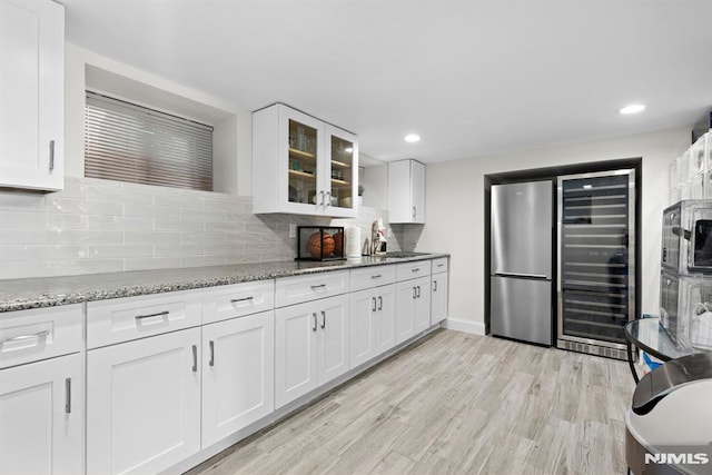 kitchen featuring white cabinets, glass insert cabinets, freestanding refrigerator, light stone countertops, and light wood-style floors