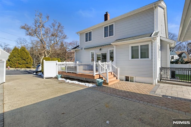 rear view of house featuring a chimney, fence, a deck, and a patio