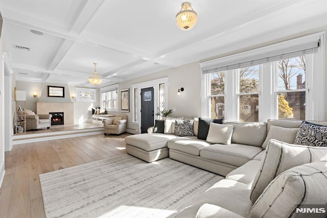 living room featuring visible vents, coffered ceiling, light wood-style flooring, a lit fireplace, and beam ceiling