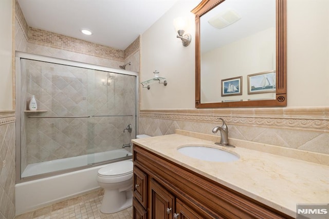 full bathroom with shower / bath combination with glass door, tile walls, vanity, tile patterned floors, and toilet