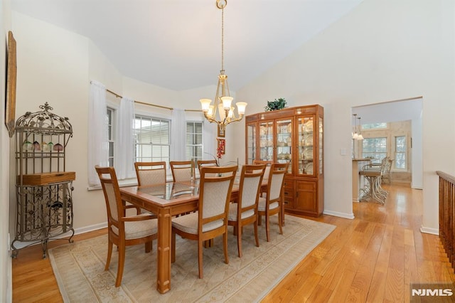 dining space featuring an inviting chandelier, high vaulted ceiling, and light hardwood / wood-style floors