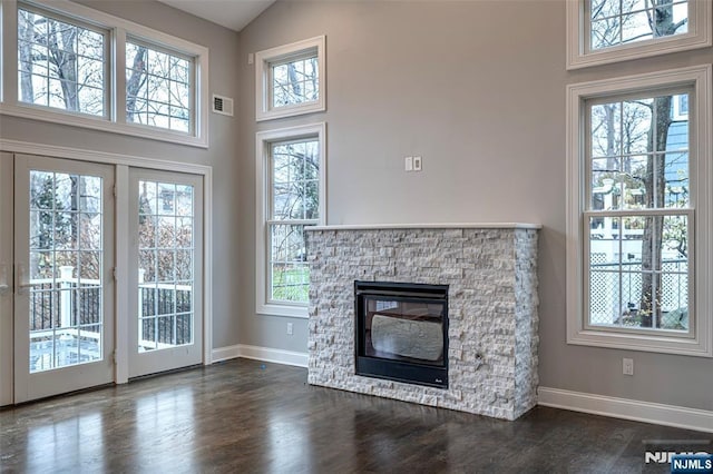 unfurnished living room with high vaulted ceiling, a healthy amount of sunlight, dark wood-type flooring, and a fireplace