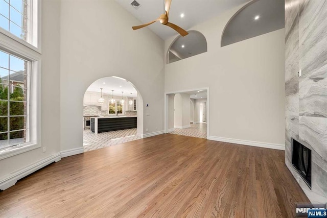 unfurnished living room with baseboard heating, wood-type flooring, a fireplace, and plenty of natural light