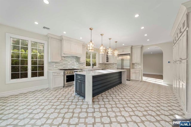 kitchen with white cabinetry, tasteful backsplash, decorative light fixtures, premium appliances, and a kitchen island