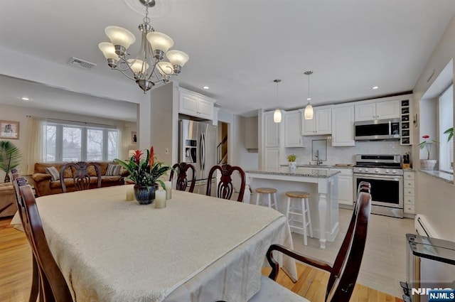 dining space featuring sink, a notable chandelier, light hardwood / wood-style flooring, and a baseboard heating unit