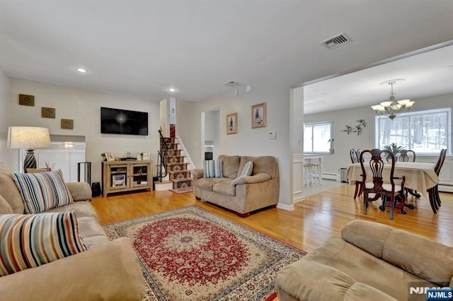 living room featuring baseboard heating, light hardwood / wood-style floors, and a notable chandelier