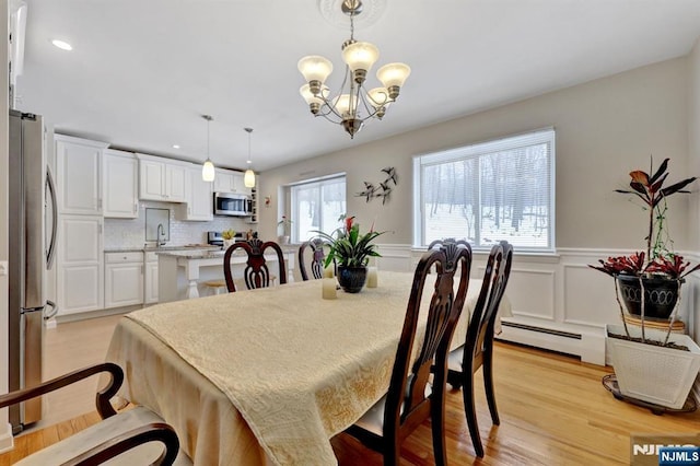 dining space with sink, a chandelier, baseboard heating, and light hardwood / wood-style flooring