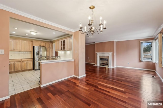 kitchen featuring a peninsula, a high end fireplace, open floor plan, stainless steel refrigerator with ice dispenser, and tasteful backsplash