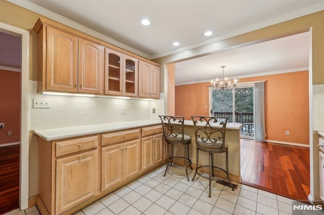 kitchen with a breakfast bar area, a peninsula, light countertops, ornamental molding, and tasteful backsplash