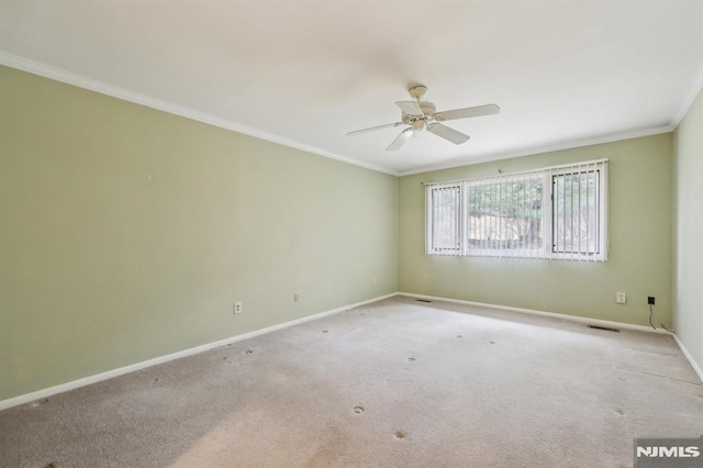 empty room with ceiling fan, carpet floors, visible vents, baseboards, and crown molding