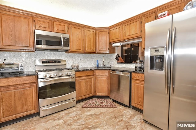 kitchen featuring stainless steel appliances, tasteful backsplash, sink, and dark stone countertops