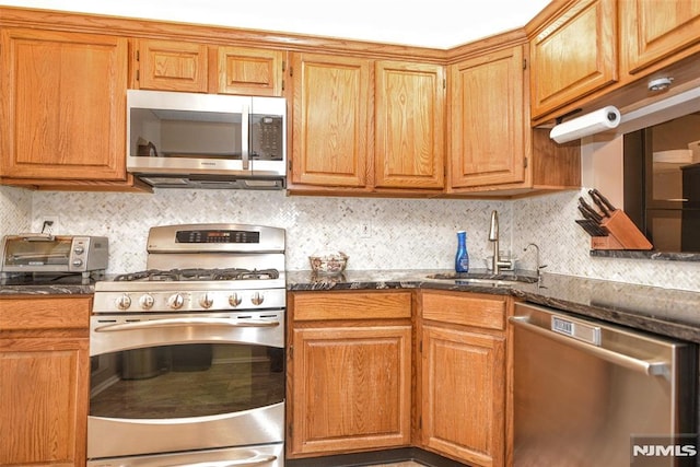 kitchen with dark stone countertops, sink, decorative backsplash, and stainless steel appliances