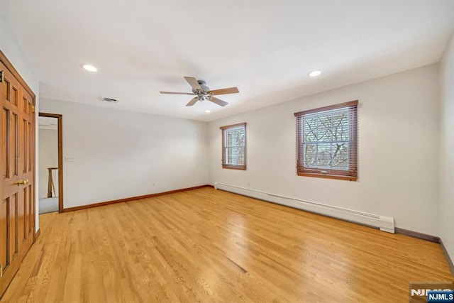 spare room featuring a baseboard heating unit, ceiling fan, and light hardwood / wood-style flooring