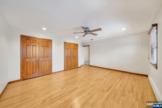 unfurnished bedroom with light hardwood / wood-style flooring, baseboard heating, multiple closets, and ceiling fan