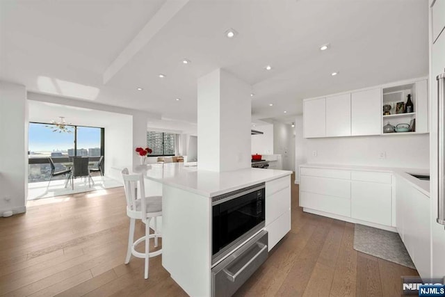 kitchen with a kitchen island, built in microwave, a breakfast bar area, white cabinets, and hardwood / wood-style flooring