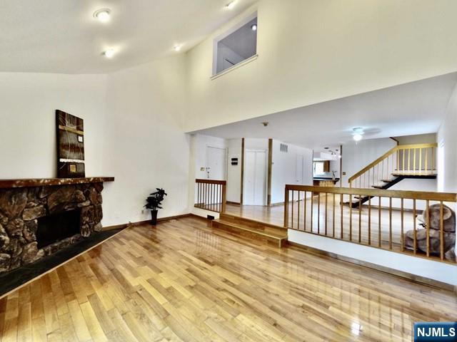 living room featuring a stone fireplace, high vaulted ceiling, and hardwood / wood-style flooring