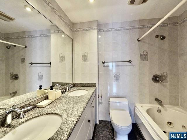 full bathroom with tile walls, vanity, tiled shower / bath combo, and toilet