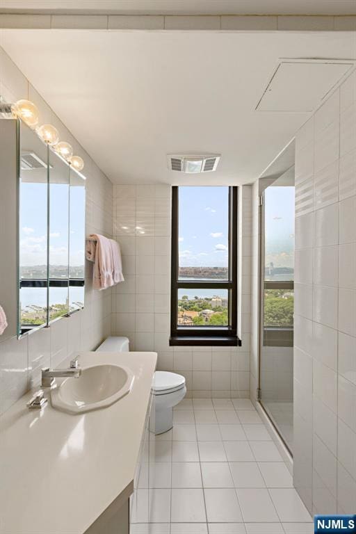 bathroom featuring tile walls, a water view, vanity, tile patterned floors, and walk in shower