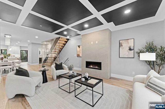 living room with a tiled fireplace, coffered ceiling, and light hardwood / wood-style floors